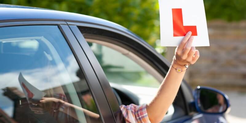 Hand holding l-plate out of car window