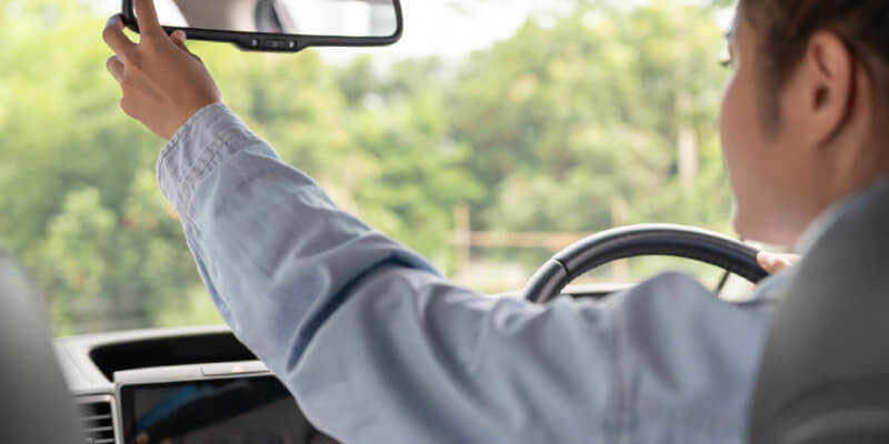 Girl reaching to adjust rear view mirror in car