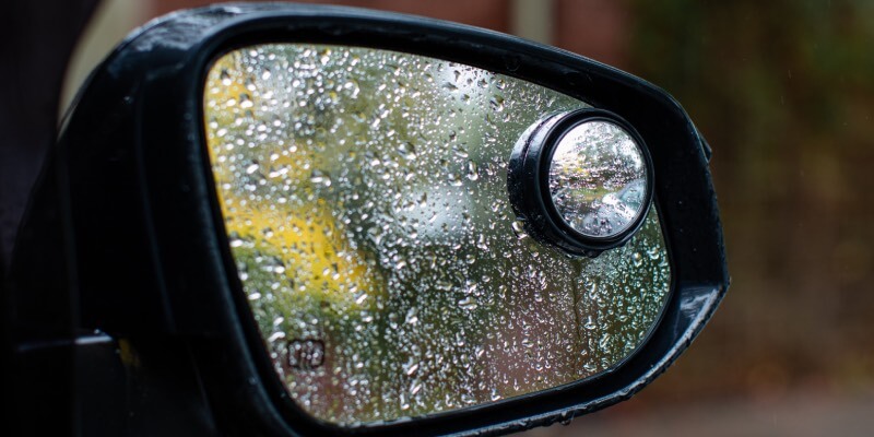 Wing mirror with blind spot mirror attached, covered in raindrops