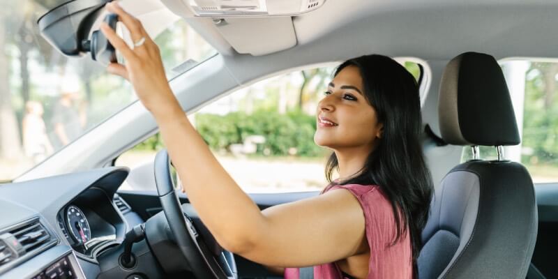 Woman reaching to adjust the rearview mirror in the car